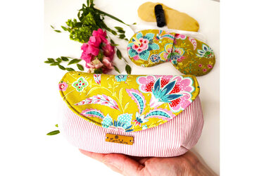 Hand hält kleine Stofftasche mit gelber, floral bedruckter Klappe und rosa-weiß gestreiftem Unterteil.