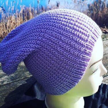 Lila gestrickte Beanie auf Schaufensterpuppe, seitliche Ansicht vor See und Schilf