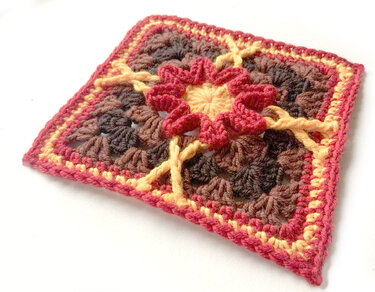 Gehäkeltes Granny Square mit gelber Mitte, roten Rüschen und braunem Hintergrund
