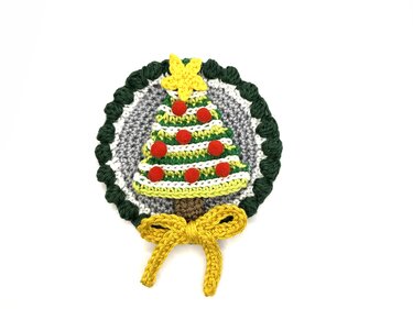 Round crocheted Christmas tree appliqué with red pom-poms, yellow star and yellow bow on grey background with green scalloped edge.