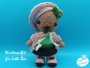 Gehäkelter Amigurumi-Bär mit lila Barett, grüner Blüte, Strickjacke, gestreiftem Oberteil, Rock und Stiefeln vor blauem Hintergrund.