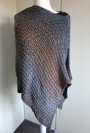 Grey-brown crocheted poncho with open mesh stitch and asymmetric pointed hem on a white mannequin