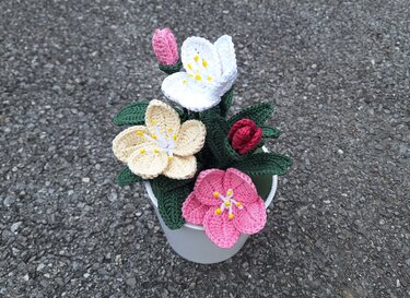 Gehäkelte Blumen in Weiß, Creme und Rosa mit grünen Blättern in einem kleinen hellen Topf