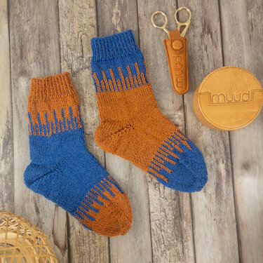 Zwei handgestrickte Socken in Blau und Rostorange mit Zackenmuster auf Holzuntergrund.