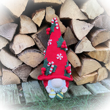 Gehäkelter Weihnachtswichtel mit roter Mütze, Zuckerstangen- und Stechpalmen-Applikationen vor Holzstapel