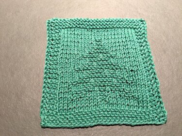 Quadratischer, türkisgrüner Strickuntersetzer mit Tannenbaum-Relief auf dunklem Hintergrund