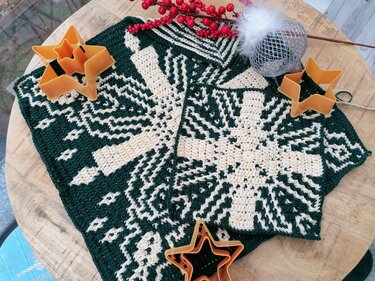 Gehäkelte Topflappen in Dunkelgrün und Creme mit sternähnlichem Muster auf Holztisch, umgeben von Ausstechern und Weihnachtsdeko