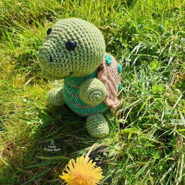 green crocheted turtle amigurumi with brown shell sitting on grass
