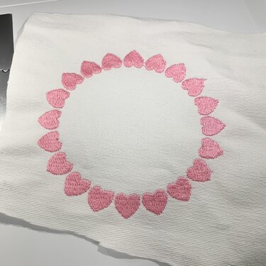 Kreisförmiger Rahmen aus rosa Herzen, auf hellem, strukturiertem Stoff gestickt