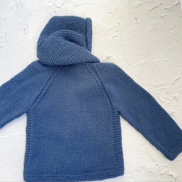 Blaue gestrickte Kinderkapuzenjacke, Rückansicht, Raglanärmel, kraus rechts an Kanten