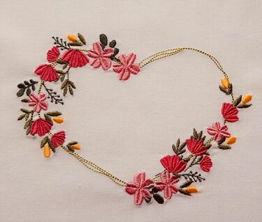 Besticktes Blumenherz mit roten und rosa Blüten auf hellem Stoff