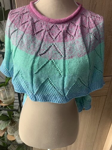Kurzärmeliges gestricktes Damenoberteil mit Farbverlauf in Pink, Mintgrün und Hellblau sowie geometrischen Lochmustern auf einer Schneiderpuppe.