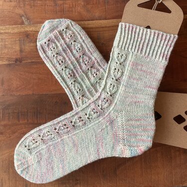 Ein Paar hell gestrickter Damensocken mit Lochmuster, liegend auf einer Holzoberfläche.