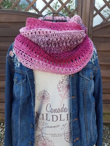 Mehrfarbiger gehäkelter Loopschal in Pinktönen auf einer Schaufensterpuppe über einer Jeansjacke
