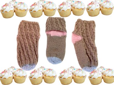 Drei gestrickte Babysocken braun mit rosa und hellblauen Akzenten, dekorative Cupcakes am Rand