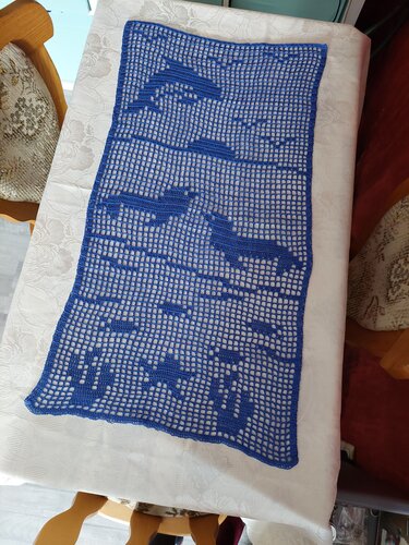 Blauer gehäkelter Tischläufer mit Delfin- und Fischmotiven auf weißem Tischtuch