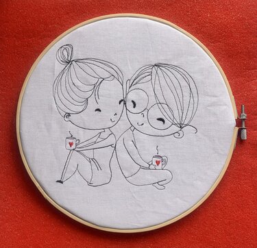 Linienstickerei im Holzrahmen: zwei sitzende Personen Rücken an Rücken mit Tassen und kleinen roten Herzen auf weißem Stoff vor rotem Hintergrund