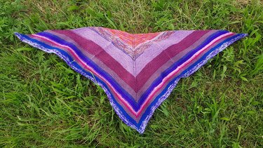 Gestricktes Dreieckstuch mit bunten Streifen in Lila, Pink und Blau auf Gras