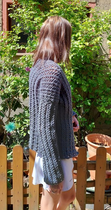 Seitliche Ansicht einer Person mit grauer, gehäkelter Damenjacke im Garten