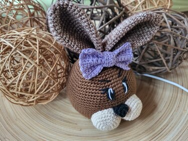 Gehäkelter brauner Hasenkopf mit großen Ohren und lila Schleife auf Holzuntergrund