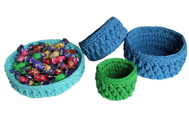 Vier gehäkelte Körbe in Türkis, Blau und Grün vor weißem Hintergrund; ein türkiser Korb gefüllt mit Bonbons.