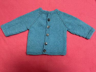 Türkise gestrickte Babyjacke mit Knopfleiste und Raglanärmeln auf pinkem Untergrund