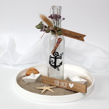 Glasflasche mit Anker‑Plott, eingerollter Nachricht, Sand, Papierbooten und Holzschild ‚Für Dich‘