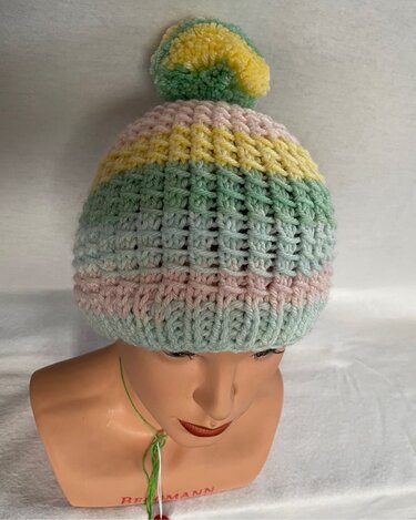 Gestreifte Strickmütze in Pastellfarben mit Bommel auf einer Schaufensterpuppe