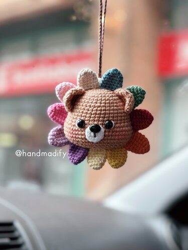 Crocheted brown bear head charm with rainbow petals hanging by a cord.