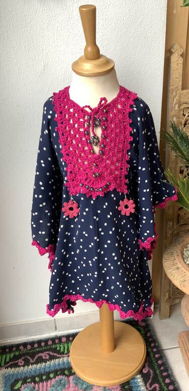 Dunkelblaues Kinderkleid mit weißen Punkten und fuchsiafarbener Häkelpasse auf Schaufensterpuppe.