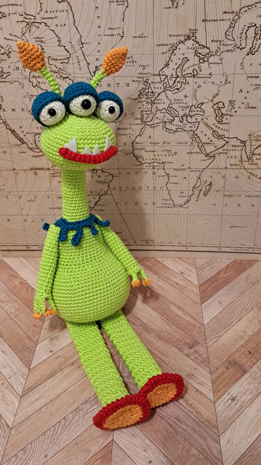 Verspieltes gehäkeltes Amigurumi-Alien, hellgrün mit drei Augen und bunten Akzenten