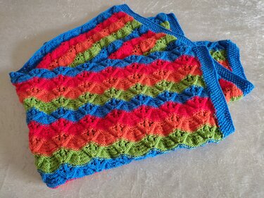 Gestrickte Babydecke mit Wellenstreifen in Regenbogenfarben und blauem Rand