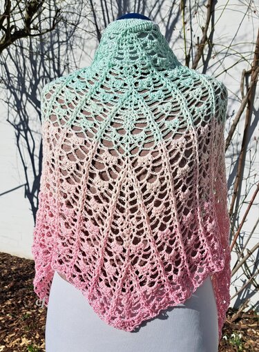 Gehäkeltes Dreieckstuch in Mint‑zu‑Rosa Ombré mit offenem Muster auf einer Schneiderbüste vor kahlen Zweigen.