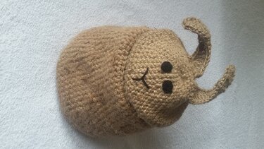 Gehäkelter brauner Korb in Käferform mit aufgesticktem Gesicht und Fühlern auf hellem Hintergrund.