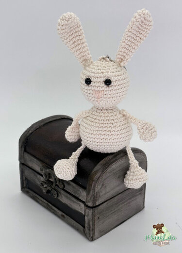 Mini-Amigurumi-Hase als Schlüsselanhänger mit Ring auf dunkler Holztruhe