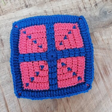 Gehäkeltes Quadrat in Blau und Pink auf Holzuntergrund, Nahaufnahme