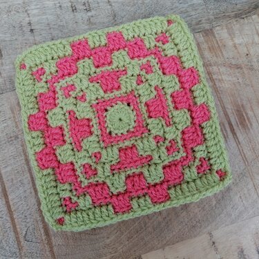 Gehäkeltes Quadrat in Hellgrün und Pink auf Holzuntergrund