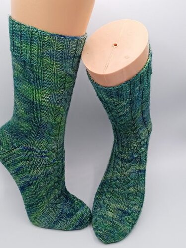 Gestrickte grün-blaue Socken mit Zopfmuster auf Schaufensterfüßen