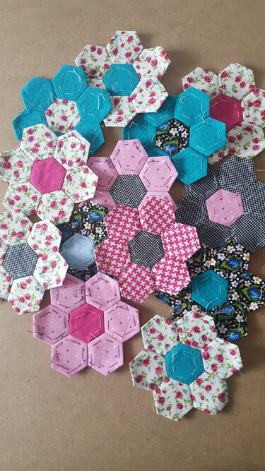 Patchwork-Blumen aus Stoffsechsecken in Rosa und Türkis mit Blumen- und Karomustern, sichtbare Handstiche
