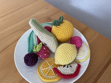 Häkel-Obst auf weißem Teller mit Birnenhälfte, Zitrusfrüchten, Apfelscheibe und Beeren