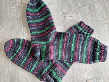 Gestricktes Paar Herrensocken in dunkelgrau mit grünen, pinken und hellblauen Streifen auf hellem Holzuntergrund