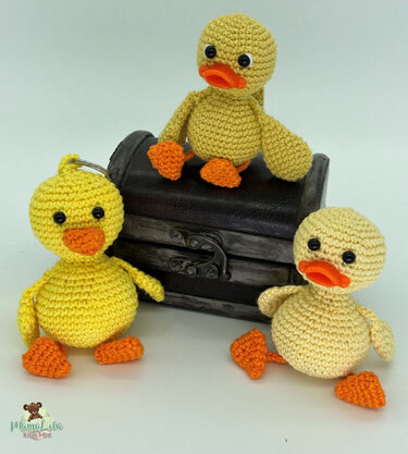 Drei gehäkelte Entchen in Gelb- und Beigetönen (Amigurumi), eines mit Schlüsselring, vor hellem Hintergrund