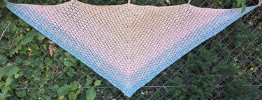 Gehäkeltes Dreieckstuch in Pastellrosa zu Hellblau mit offenem Lochmuster, aufgehängt an Drahtzaun