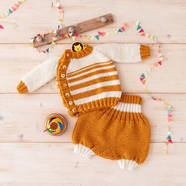 Gestricktes Baby-Set in Senfgelb und Cremeweiß mit gestreiftem Cardigan und Pumphose auf hellem Holz