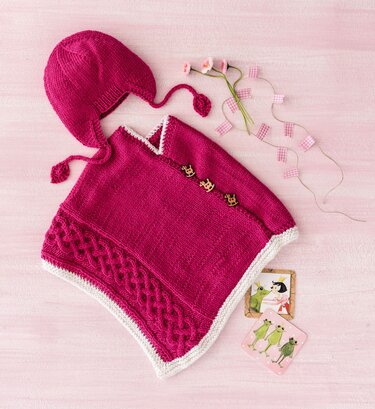Himbeerroter Baby-Poncho mit Zopfmuster, Holzknöpfen und passender Ohrenschützer-Mütze mit Bindebändern