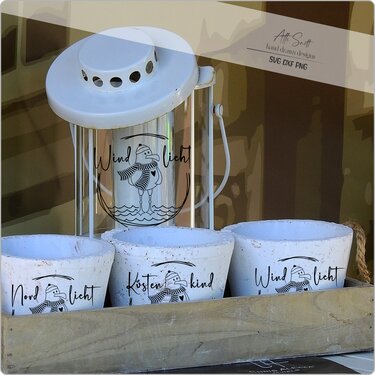 Weiße Laterne und drei weiße Tontöpfe mit schwarzem, maritimem Plotmotiv eines Vogels mit Mütze und den Schriftzügen Windlicht, Nordlicht und Küstenkind