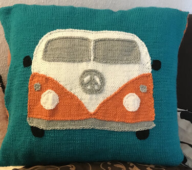 Türkises gestricktes Kissen mit aufgenähtem Campingbus-Motiv in Weiß, Orange und Grau mit Friedenszeichen.