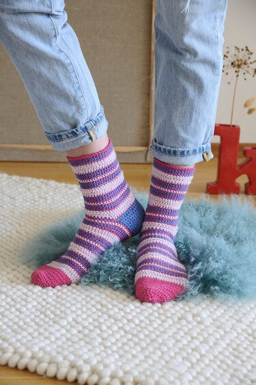 Gehäkelte, gestreifte Damensocken in Pink, Hellrosa und Violett mit blauer Ferse auf hellem Teppich