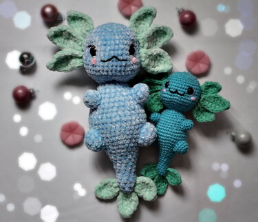 Zwei blaue gehäkelte Amigurumi-Wasserwesen mit fransigen Kiemen, liegend