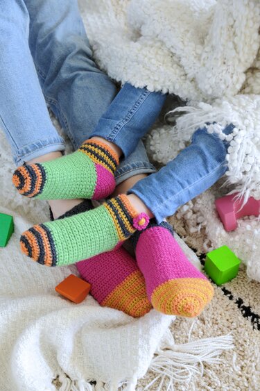 Kinderbeine in gestreiften, gehäkelten Socken auf einer flauschigen Decke neben Holzbauklötzen.